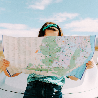 Woman reviews a paper map while leaning against the hood of a white vehicle