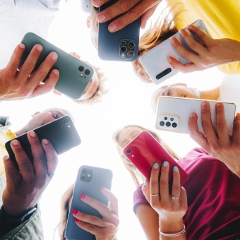 Seven individuals holding cell phones of differing colors in a circle