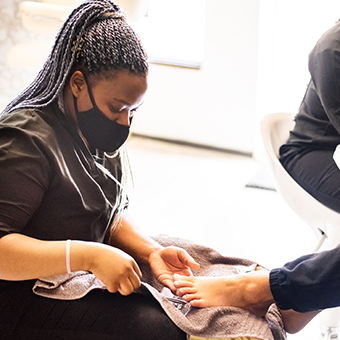 Masked esthetician performing a pedicure service
