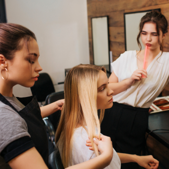 Cosmetologist examines a client's blonde hair while being supervised