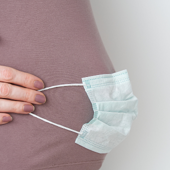 An image of pregnant woman with face mask on abdomen